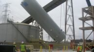 Construction workers surveying a silo being set by crane