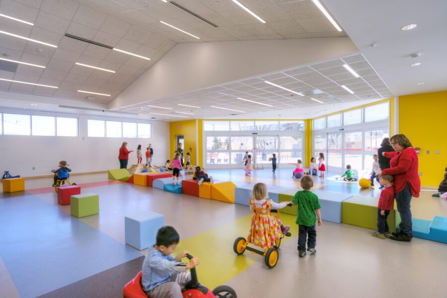Childhood Care Center with open play area. Colorful blocks and bikes fill the space with children playing. K12 Education