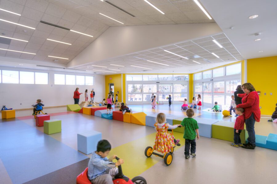 Childhood Care Center with open play area. Colorful blocks and bikes fill the space with children playing. K12 Education