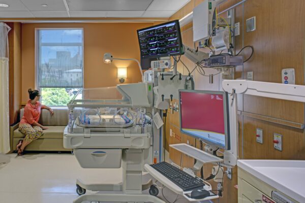 Woman looking out window in NICU patient room with medical equipment