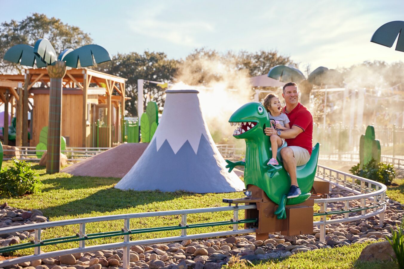 A father and his daughter ride the miniature green dinosaur through the prehistoric land